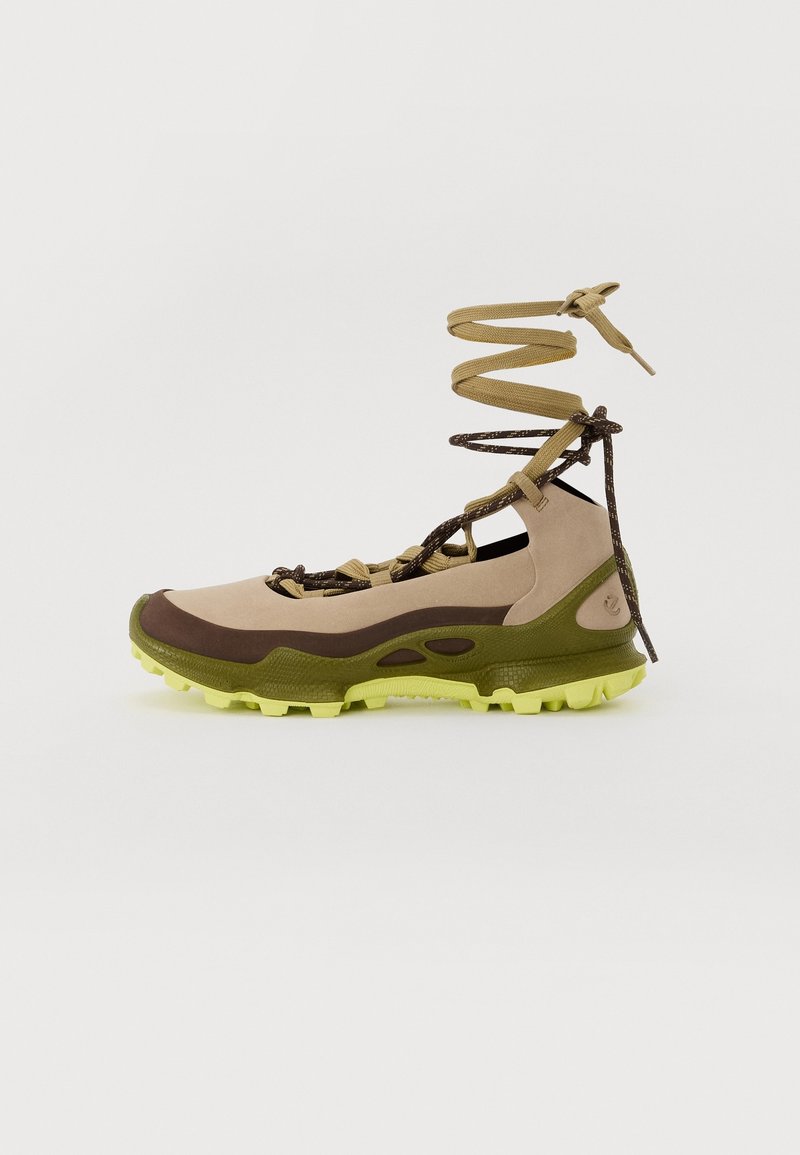 Chaussure de randonnée beige, marron et verte avec semelle vert citron et lacets bicolores enroulés vers le haut pour soutenir la cheville sur fond blanc uni.