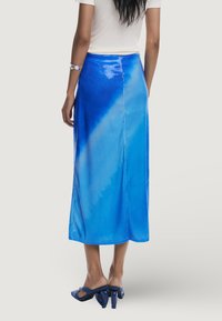 Blaue Pailletten-Rock mit einem Farbverlauf-Design, midi-länge, glatte Textur und einem seitlichen Schlitz. Kombiniert mit blauen Absatzschuhen.