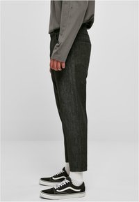 Un pantalon en denim gris foncé présente une coupe droite, un tissu texturé et un design classique à cinq poches ; associé à des baskets noires et des chaussettes blanches.