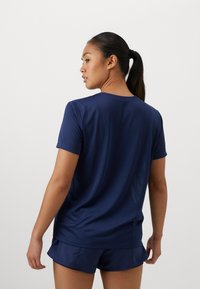 Námořnické modré sportovní tričko, těsně obepínající, krátké rukávy, hladká textura, kulatý výstřih, nošené s odpovídajícími šortkami. Pohled na zadní stranu oděvu.