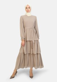 Beige flerlagad klänning med långa ärmar och midjebälte. Tillverkad av lättviktig tyg med mjuk textur. Matchad med beiga klackar.