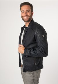 Giacca in pelle nera con colletto alto, chiusure con zip e finitura texturizzata. Presenta dettagli sulle spalle e tasche laterali.