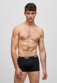 Black boxer briefs with a white "BOSS" logo on the elastic waistband; model with a muscular build and short, textured hair.