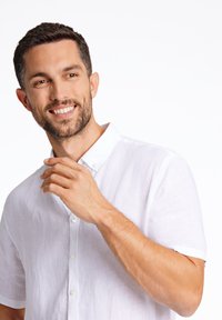 Witte linnen overhemd met korte mouwen en een button-down kraag, met een subtiele textuur en een relaxte pasvorm, gedragen door een man die zijn kraag vasthoudt.