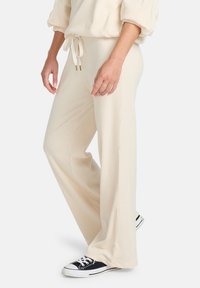Beige geribde loungebroeken met een hoge taille en een trekkoord, met een relaxte pasvorm en brede benen. Gdraagd met zwarte sneakers.
