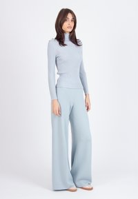 Svetlo modra rebrasta turtleneck pulover, v kombinaciji s širokimi trenirkami, oboje v mehkem materialu, ki se dopolnjujeta tako v barvi kot v oblikovanju.