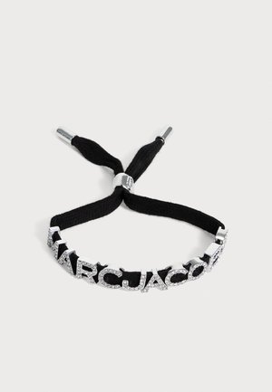 Bracelet en tissu noir avec des lettres en argent incrustées de cristaux formant le mot "MARC JACOBS" et des extrémités de fermoirs coulissants en métal réglables.