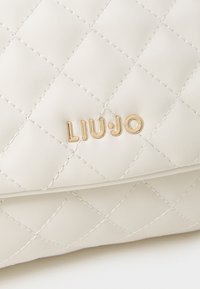Zgibana bela torba iz sintetičnega usnja z zlatim logotipom "LIU JO". Ima izbočene šive in gladko teksturo. Kompaktna pravokotna oblika.