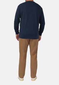 Langarm-Navy-T-Shirt mit Rundhalsausschnitt, kombiniert mit khakifarbenen Hosen und weißen Sneakers. Es hat einen lockeren Schnitt und eine weiche Stoffstruktur.