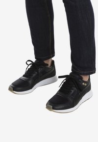 Sneaker sportive nere con una parte superiore tessurizzata, suola intermedia bianca e lacci neri. Presenta un logo dorato discreto sul lato.