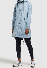 Parka impermeabile azzurro chiaro con cappuccio, bottoni neri a contrasto e tasche frontali. Presenta un cordoncino regolabile all'orlo e una patch con logo.