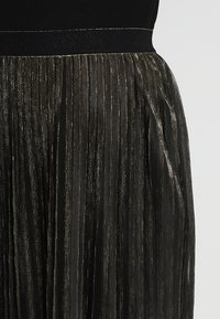 Jupe plissée noire avec des fils métalliques dorés, dotée d'une taille élastique lisse et d'un tissu texturé et fluide.