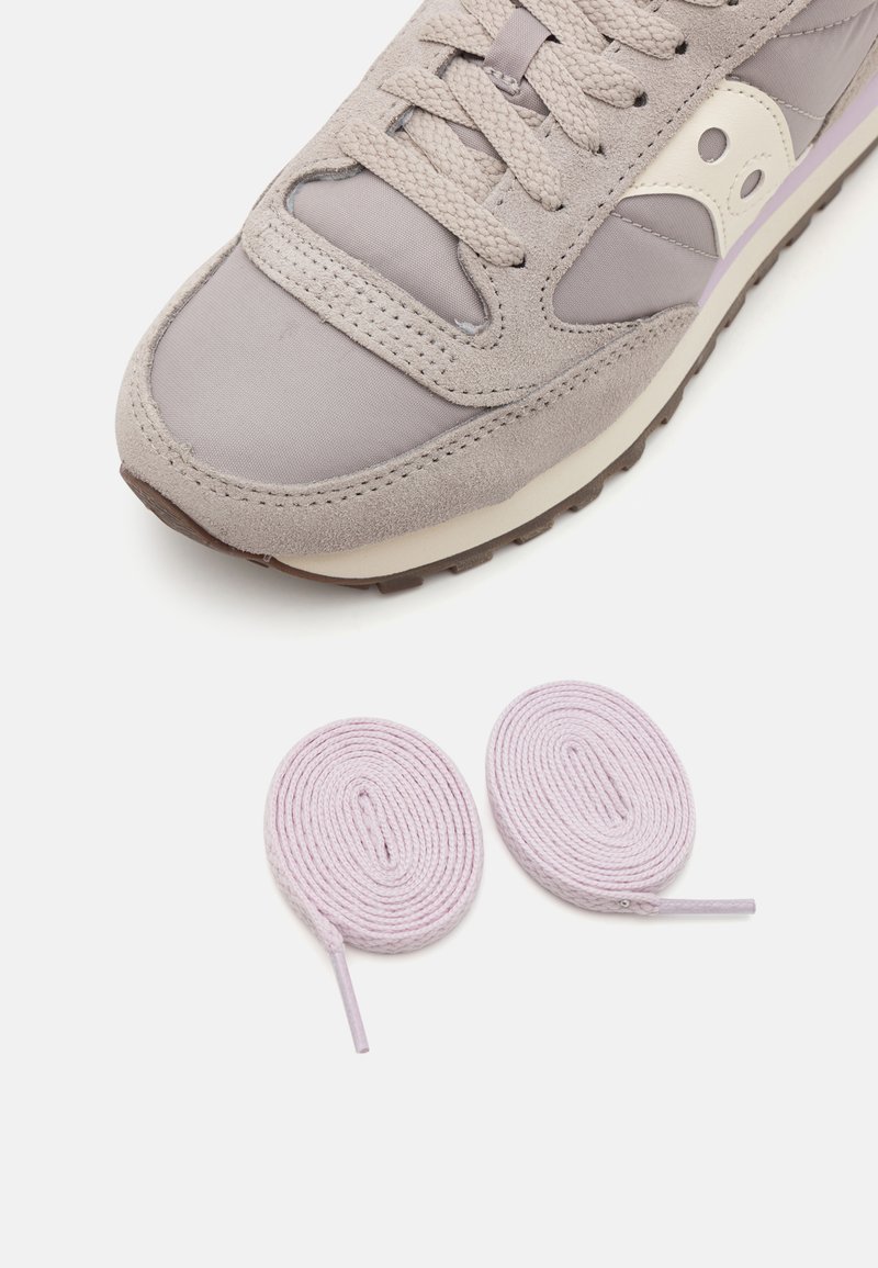 Sneaker grigio in suede e tessuto con suola crema e accenti lilla chiaro, accompagnato da due lacci arrotolati di colore lilla.