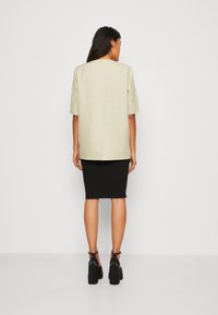 Ljust beige kortärmad topp med rak skärning, tillsammans med en figurnära svart knä-lång kjol, kompletterad med blockklackade svarta sandaler.