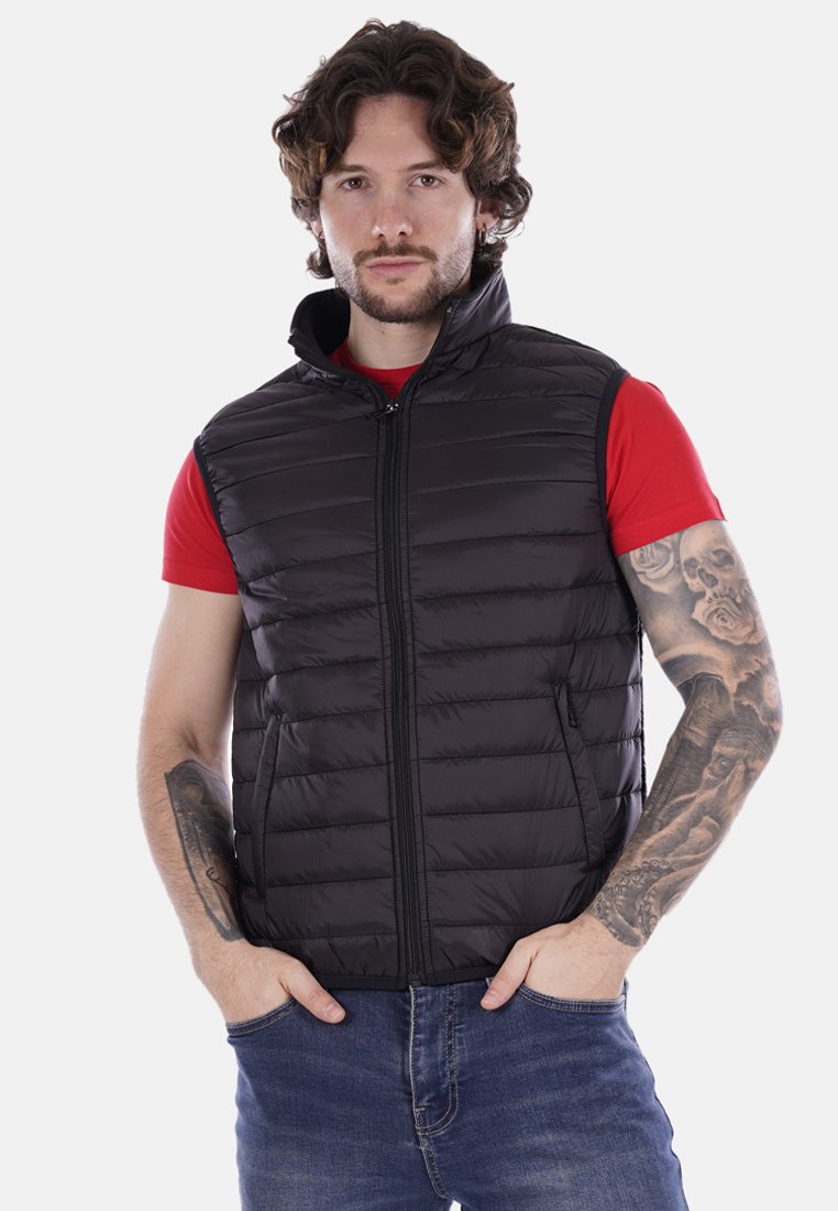 Gilet imbottito nero con collo alto, chiusura frontale con zip e tasche laterali. Indossato sopra una maglietta rossa, con modelli a righe orizzontali.