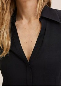 Chemise noire à col en V avec un col structuré, présentant un design élégant, une texture lisse et des détails de couture subtils.