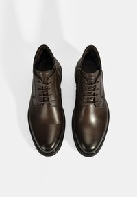 Chaussures habillées en cuir marron avec une finition lisse et brillante, dotées de lacets et de légères surpiqûres, sur fond blanc.