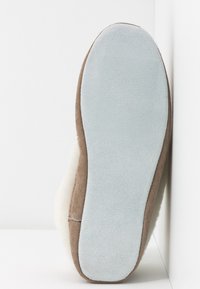 Brown suede slipper bottom with light blue velvety sole and white fur lining. Rounded shape with seam details along the edges.