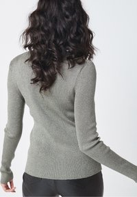 Pull côtelé vert olive avec accents métalliques, doté de manches longues et d’une coupe ajustée, présentant une surface texturée.