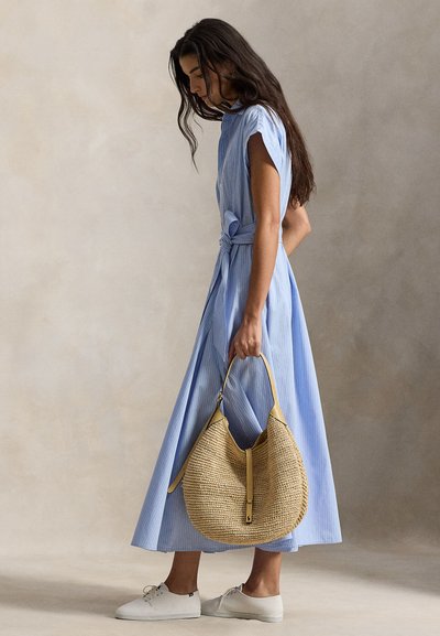 Φόρεμα με γαλάζιες ρίγες, με ζώνη δέσιμη στη μέση, συνδυασμένο με πλεκτή καφέ τσάντα και λευκά παπούτσια. Το φόρεμα έχει άνετη γραμμή και κοντά μανίκια.