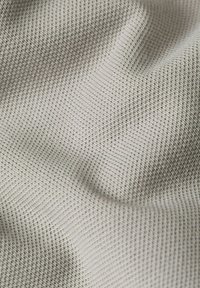 Teksturowana dzianina w jasnoszarym kolorze, z gęstym wzorem małych wypukłych kwadratów. Miękka i gładka powierzchnia, o lekko pomarszczonym wyglądzie.