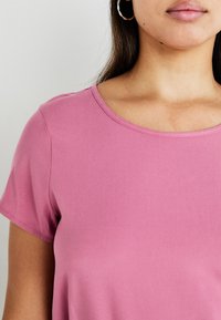 Rosa kortermet topp med rund hals, laget av glatt stoff. Har rene sømmer og en tettsittende stil rundt kragen.