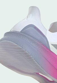 Bílé sportovní tenisky s designem připomínajícím ponožku, růžovými a šedými akcenty, flexibilní mezipodešví a texturovanou gumovou podešví se vzorovaným gripem.