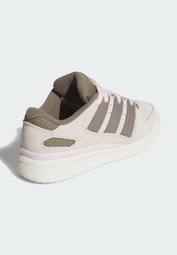 Beige suede sneaker with pink laces and accents, textured mesh side, three brown stripes, and a white rubber sole with branding.