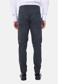 Pantaloni tailored grigio scuro con una texture di tessuto liscia, tasche posteriori con zip e design a gamba dritta, abbinati a scarpe nere lucide.