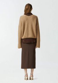 Maglione a coste beige indossato su una gonna aderente marrone, con colletto marrone decorato e sandali con tacco argento.