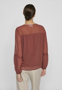 Bordeaux genomskinlig blus med strukturerade prickar, långa ärmar med rynkade manschetter och en ryggslits för lös passform.