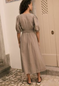 Robe longue en lin dans un taupe atténué avec des manches bouffantes et une taille smockée, présentant une silhouette droite et un ourlet au niveau du genou.