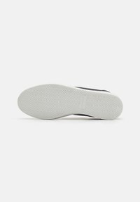 Sneaker nera con suola in gomma testurizzata con motivo a spina di pesce e dettagli bianchi. Il design presenta una forma elegante e affusolata.
