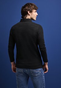 Czarna, długorękawowa koszulka polo z teksturowanej tkaniny, dopasowany krój i płaski kołnierzyk, w połączeniu z niebieskimi dżinsami.