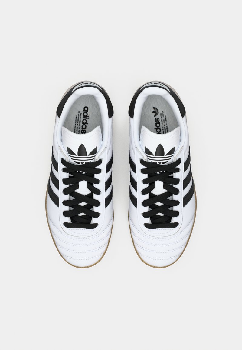 Weiße Ledersneaker mit drei schwarzen Streifen, schwarzen Schnürsenkeln und einer strukturierten Sohle. Mit einem klassischen Logo auf der Zunge.