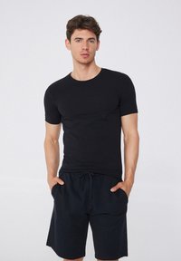 Černé tričko s krátkým rukávem vyrobené z měkké tkaniny, s kulatým výstřihem. Slučuje se s černými šortkami na stažení v pase, které mají boční kapsy.