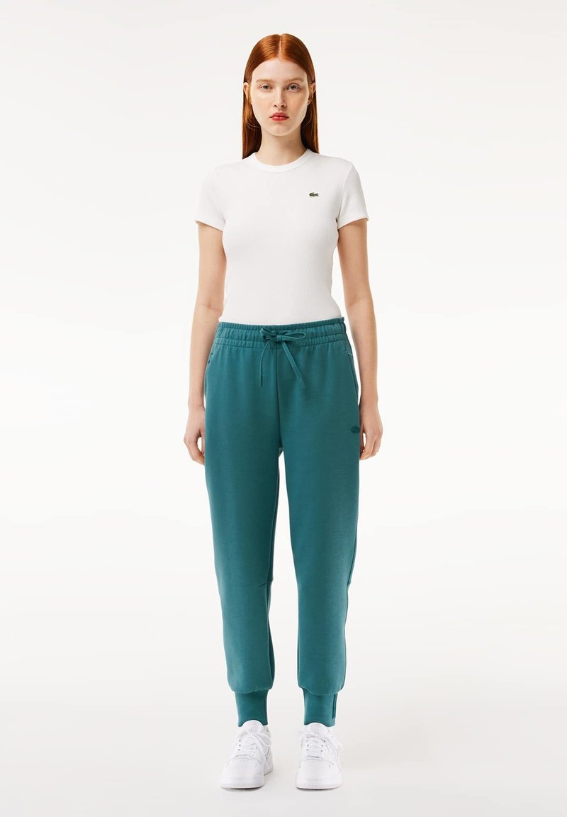 Biała, prążkowana koszulka z krótkim rękawem i turkusowe dresy z elastycznymi mankietami, z troczkiem w pasie i małym logo na biodrze.