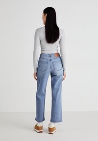Light blue high-waisted jeans with a relaxed fit, denim texture, and back pockets; paired with a fitted gray long-sleeve top and tan sneakers.