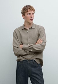 Beige linen button-up shirt with a chest pocket, paired with dark blue denim jeans. Features long sleeves and a relaxed fit.