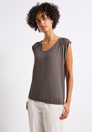 Haut sans manches gris foncé avec un décolleté en V, texture douce, détails froncés aux épaules, associé à un pantalon clair et ample.
