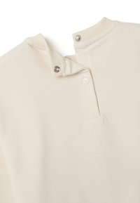 Prenda de manga larga color crema con cuello acanalado y cierre a presión. Textura suave con un diseño sutil y minimalista.