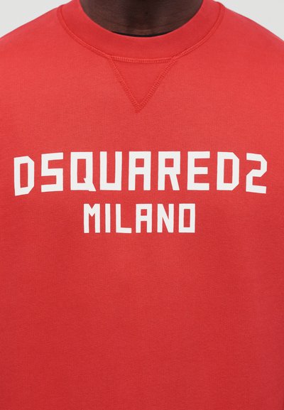 Sudadera roja con texto blanco "DSQUARED2 MILANO" en el pecho, llevada por una persona de piel oscura, recortada a la altura del cuello y los hombros.