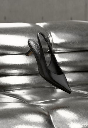 Μαύρο μυτερό παπούτσι slingback με γυαλιστερό δερμάτινο φινίρισμα, με χαμηλό τακούνι τύπου block και λεπτό λουράκι στον αστράγαλο, αιωρούμενο πάνω από μια μεταλλική επιφάνεια.
