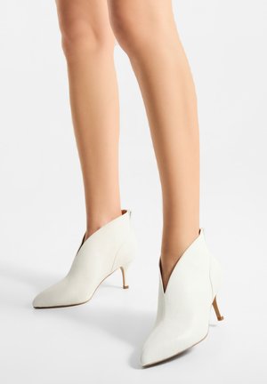 Bottines blanches en cuir avec un bout pointu et un dessus en forme de V unique. Elles présentent un talon fin et une texture lisse.