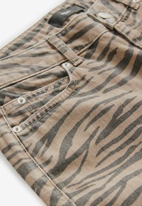 Brown denim pants featuring a black tiger stripe pattern, with silver hardware, stitching details, and a standard five-pocket design.
