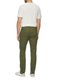 Olijfgroene broek van katoen met een rechte snit, twee achterzakken, gedragen met een wit t-shirt met korte mouwen en sneakers.