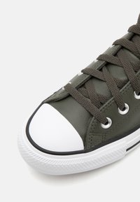 Grön lädersneaker med en vit gummitå, texturerad sula och bruna snören, med silveröglor och en klassisk design.