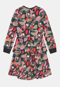 Robe à manches longues arborant des motifs géométriques multicolores en rouge, rose, vert et beige. Confectionnée en tissu doux avec une jupe à volants.