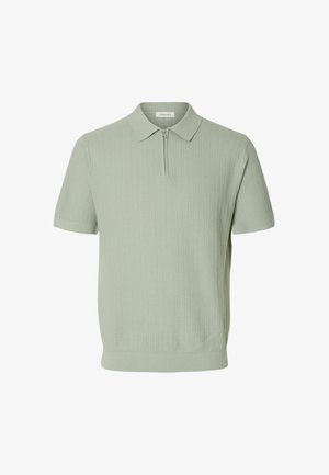 Polo de manga corta de color verde claro con textura acanalada, que presenta un cuello y un cierre de media cremallera en la parte delantera.