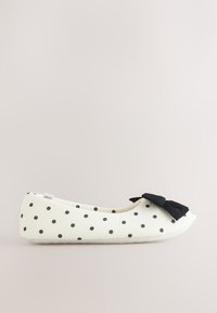 Ballerine plate blanche à pois noirs avec un nœud noir sur le bout, vue de profil sur un fond neutre.